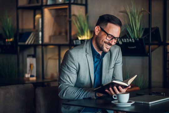Smiling businessman reading notes in cafe enjoying a coffee - Powered by Adobe