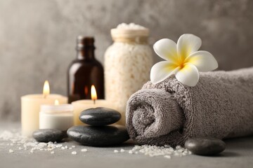Spa arrangement rolled towel flower stones candles oil bottle jar with bath salts on grey backdrop