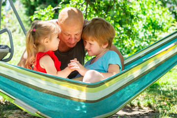Cheerful family, grandfather and grandchildren relaxing outside in the park, children sitting in the hammock 