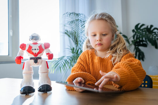 Girl using tablet PC by robot on table at home