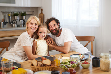 Parents and their daughter share a joyful moment at the dining table filled with delicious food, surrounded by a warm and inviting kitchen atmosphere.