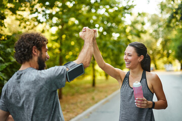 Two friends show excitement and camaraderie after their workout in a lush green park during a sunny day, representing a commitment to fitness and a healthy lifestyle.