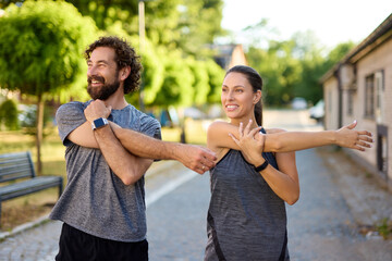 Two individuals engage in stretching exercises at a park on a sunny day, enhancing their fitness routine as they enjoy the outdoors together. The atmosphere encourages a healthy lifestyle.