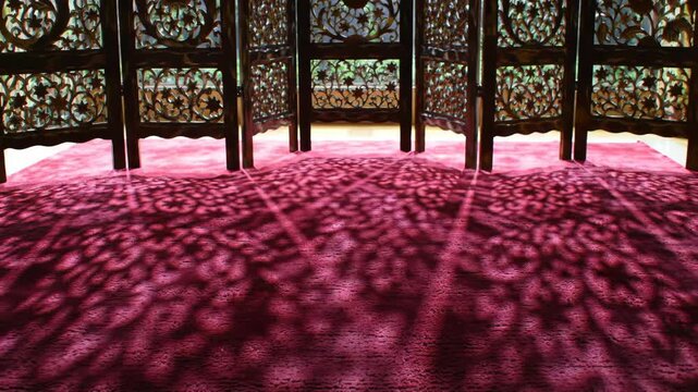 Intricate wooden screen casting floral pattern shadow on pink rug indoors, creating unique patterns and design.