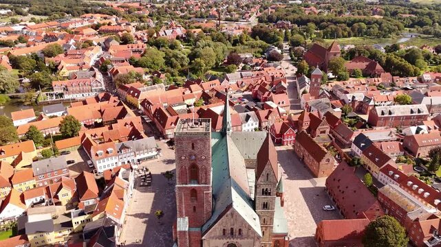 Aerial view of the Ribe Cathedral, surrounded by a sea of red rooftops, creating a visually striking contrast against the lush greenery, Ribe, Denmark.