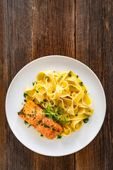 Pasta with baked salmon steak on wooden table	