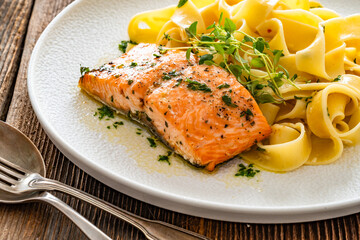 Pasta with baked salmon steak on wooden table	