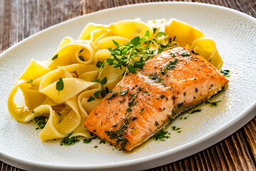 Pasta with baked salmon steak on wooden table	