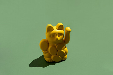 Yellow Maneki neko lucky cat figurine on green background with copy space