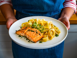 Woman holding plate with pasta with baked salmon steak, close-up