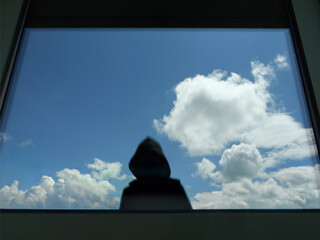 Dark Figure in Hoodie, Silhouette In Front Of A Window Looking At A Cloudy Sky