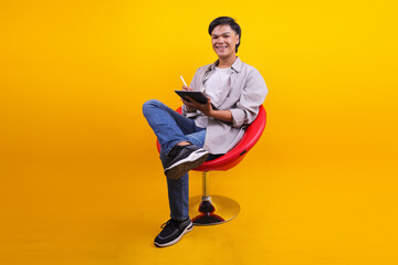 Smiling Young Asian Man Working On Digital Tablet Isolated On Yellow Background