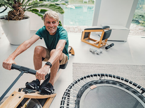 Smiling man rowing on machine during home fitness workout in living room
