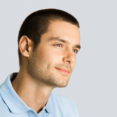 Portrait of happy smiling young brunette hair thinking man, wear blue polo shirt, isolated against grey gray wall background. Square image