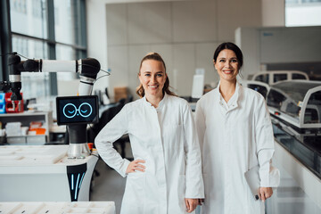 Two scientists in lab coats working with robot in modern laboratory