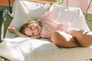 Child relaxing on garden swing with golden curls in soft sunlight