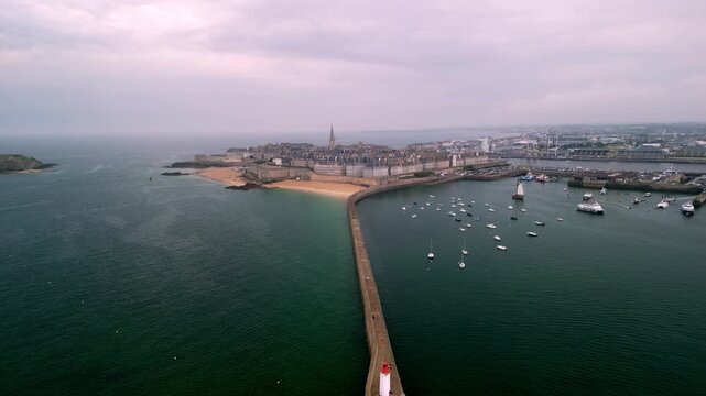 Aerial view of Saint-Malo's walled city embraced by the sea, a symphony of blues and greys punctuated by the white sails of boats, Saint-Malo, Brittany, France.