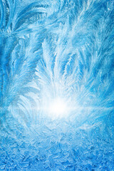 Frost patterns on frozen window illuminated by sunlight. Bright sun shines through icy texture, creating cold winter atmosphere. Image evokes winter season and low temperatures.