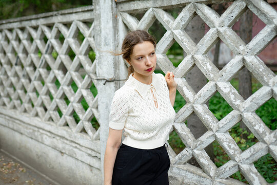 Portrait of a woman in a lace blouse standing by a patterned fence outdoors