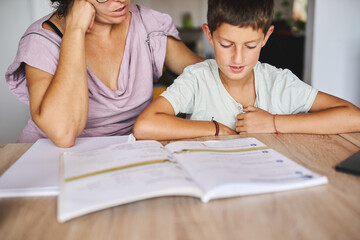 Mother helping young boy with homework at home, learning and studying together
