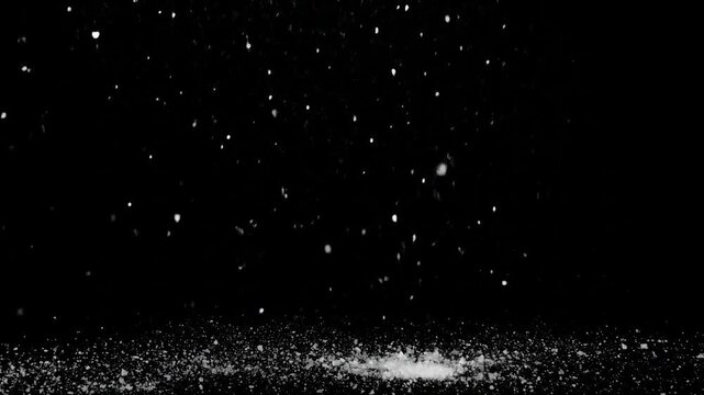White particles fall against a black background, gathering on the floor