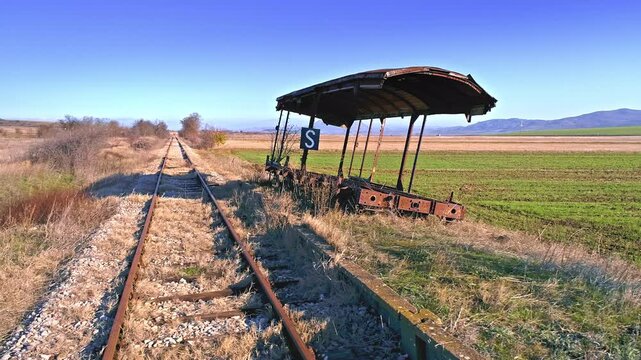 Old damaged rusty wagon, station sign, fields by the railroad
