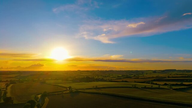 Sunset time lapse with glowing sun over agricultural countryside landscape captured from drone. Evening timelapse with dramatic orange sky and rolling farmland aerial view. Golden hour with bright
