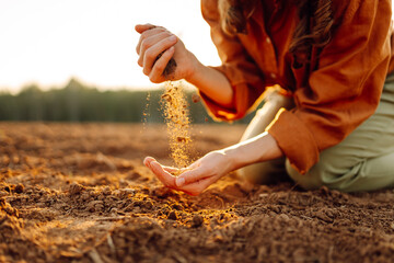 An experienced farmer kneels in a plowed field, letting the soil fall through his fingers. An...