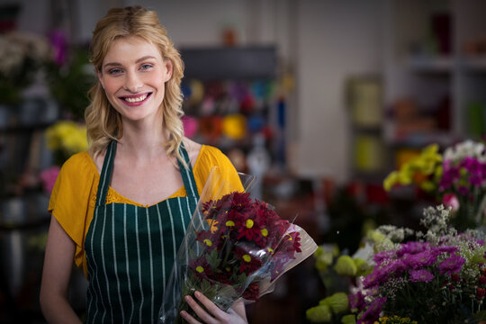 Florist holding wrapped yellow-centered red chrysanthemums amid shelves of vases, buckets, ribbons
