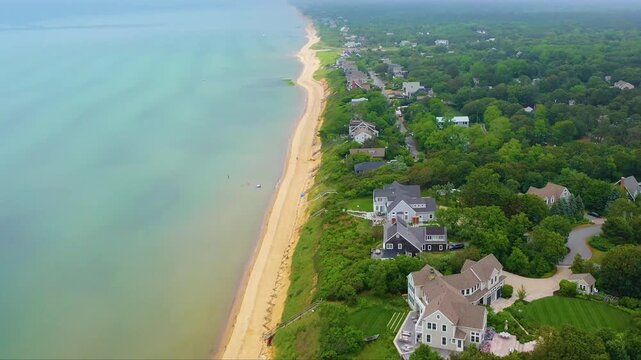 High aerial view of Cape Cod shoreline lined with beach houses, beneath low gray clouds and drifting mist, creating a dramatic seascape where coastal architecture and rugged nature meet at once.