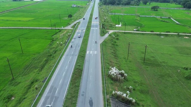 Aerial view of a straight highway cutting through lush green fields, with vehicles moving along the asphalt, Bundu, Jharkhand, India.