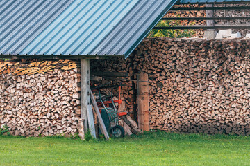Wheelbarrow leaning against stack of split firewood on a farm, rustic farm scene