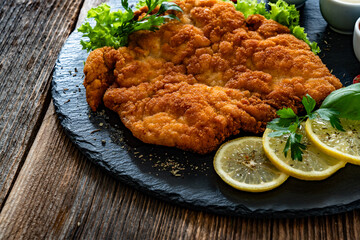 Garnished wiener schnitzel with ketchup, mayonnaise and mustard on wooden table