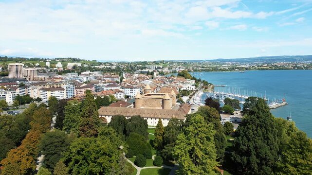 Aerial view of Morges Castle and the harbor, with its many docked boats, contrasting with the lush green trees and blue water, Morges, Vaud, Switzerland.