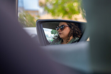 Woman driving car wearing sunglasses reflected in side mirror