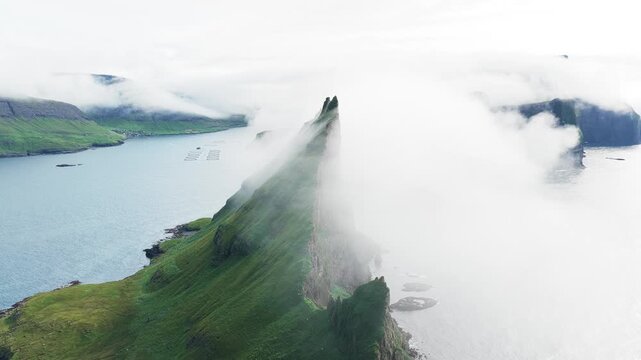 Aerial view of the dramatic, verdant Tindh&oacute;lmur island, partially veiled in ethereal mist, contrasting with the serene blue waters, Tindh&oacute;lmur, Faroe Islands.