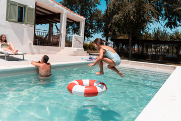Girl jumping in swimming pool with family during summer vacation