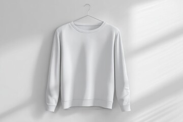 A white long-sleeved hoody made from thick cotton fabric hangs neatly against a plain wall. Soft, natural light illuminates the texture and color of the garment