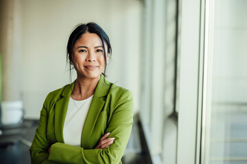 Confident businesswoman in green suit standing by office window