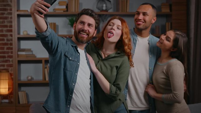 Funny four multiracial friends make selfie photo together posing grimacing smiling happy cuddling photographing recording video on mobile phone diversity people at home party men women take picture