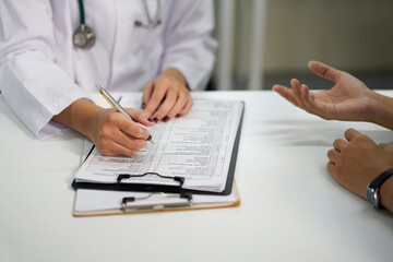 Fototapeta premium Unknown doctor and patient talking while sitting at the desk in hospital office, close-up of human hands. Medicine and health care concept