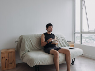 Fototapeta premium Man is sitting on a couch with a bowl of food in his hand