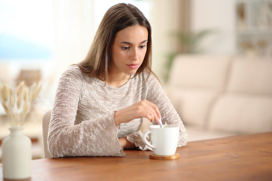 Distracted and pensive woman stirring coffee at home
