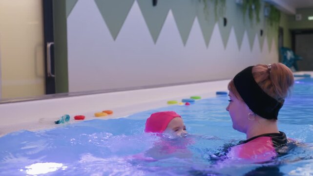 plump baby flinches from water splash near pool edge, wide eyes, hands raised for comfort, soft cheeks wet, first swim lesson vibe, caregiver nearby offering reassurance, gentle ripples, warm light