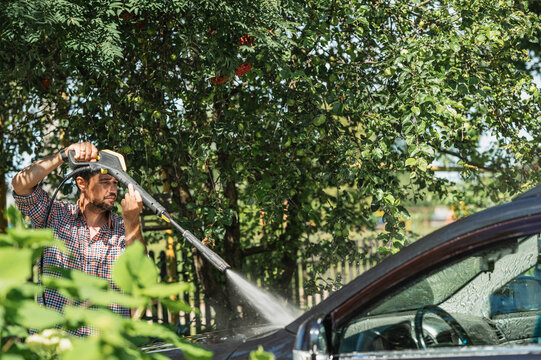 Driver washing car outdoors in summer next to green trees