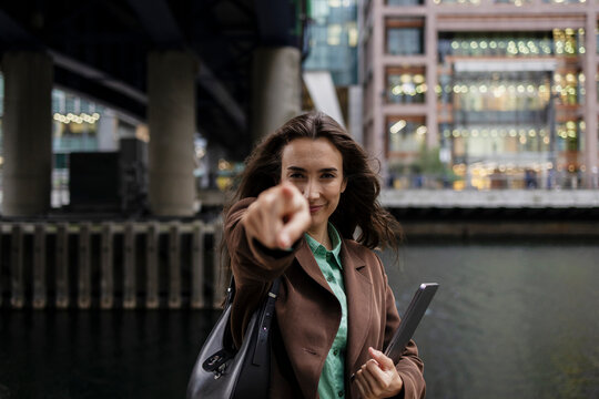 Businesswoman pointing at camera with tablet by urban canal