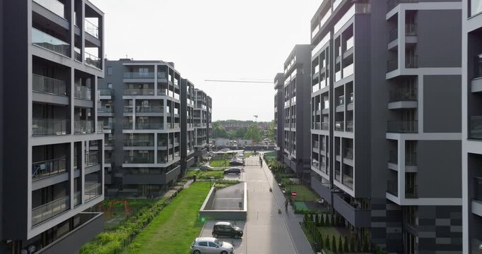 Low-altitude drone shot between modern apartment buildings in Krak&oacute;w, Poland, showing glass balconies, parking spaces, and landscaped areas, highlighting contemporary urban residential design.