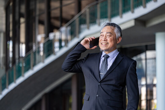 Senior business asian man is talking to mobile phone in his modern office for professional disscussion usage