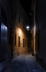 Fototapeta premium A dark alleyway of an ancient medieval town with a street light shining on it