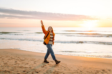 A beautiful woman with a backpack strolls along the shore at dawn. The traveler enjoys the seascape in the sun's rays. Concepts of travel, enjoyment, and freedom.